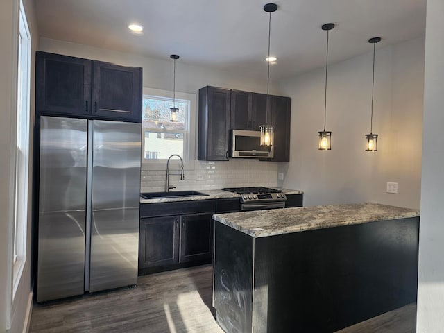 kitchen with light stone counters, dark wood-style flooring, a sink, decorative backsplash, and appliances with stainless steel finishes