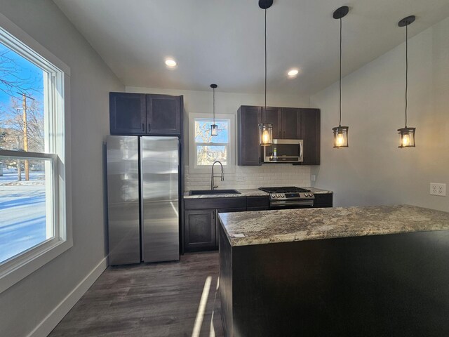 kitchen featuring light stone counters, baseboards, a sink, decorative backsplash, and stainless steel appliances