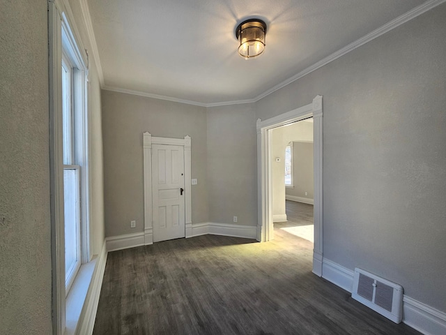 empty room featuring crown molding, wood finished floors, baseboards, and visible vents