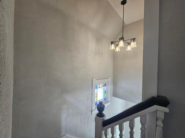 stairs featuring a textured wall, an inviting chandelier, and vaulted ceiling