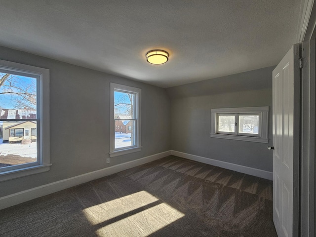 empty room featuring baseboards, a textured ceiling, and dark carpet