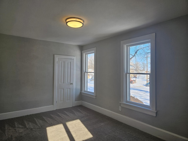 empty room with dark colored carpet, baseboards, and plenty of natural light