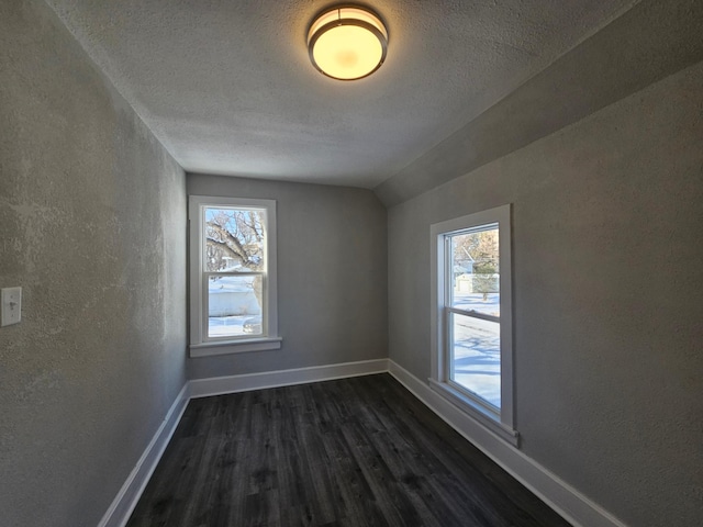 unfurnished room with dark wood finished floors, a textured wall, baseboards, and a wealth of natural light