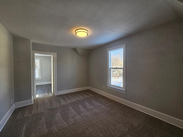 unfurnished room featuring a textured ceiling, a healthy amount of sunlight, dark colored carpet, and baseboards