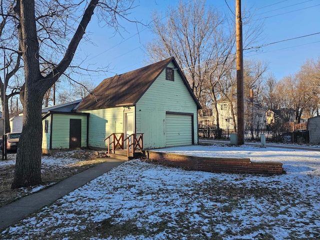 snow covered garage with driveway and a detached garage