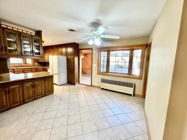 kitchen featuring radiator heating unit, ceiling fan, light stone countertops, light tile patterned flooring, and white refrigerator