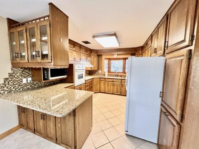 kitchen with white appliances, tasteful backsplash, kitchen peninsula, light stone counters, and light tile patterned floors