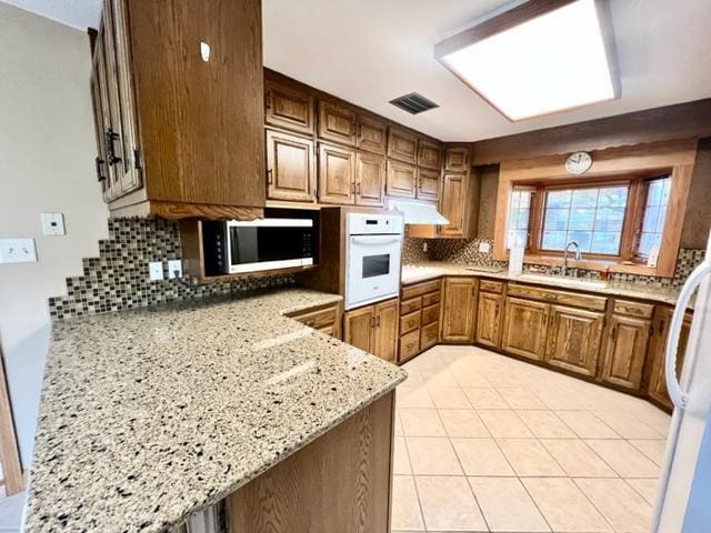 kitchen with backsplash, sink, light stone countertops, light tile patterned floors, and white appliances