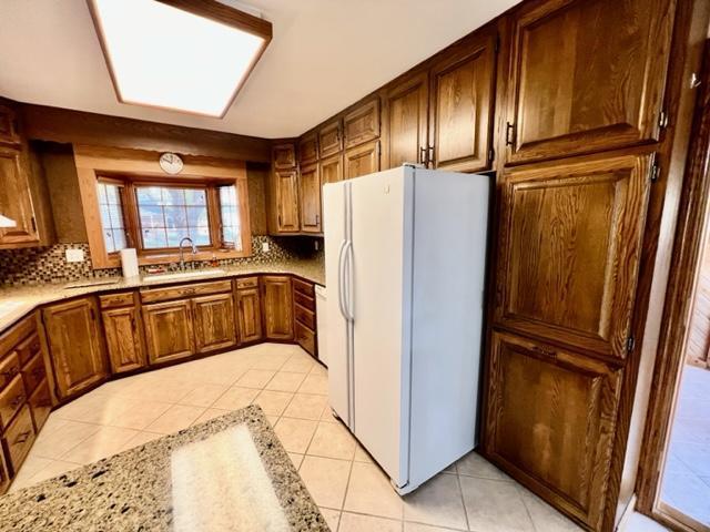 kitchen with tasteful backsplash, sink, a skylight, white refrigerator with ice dispenser, and light tile patterned floors