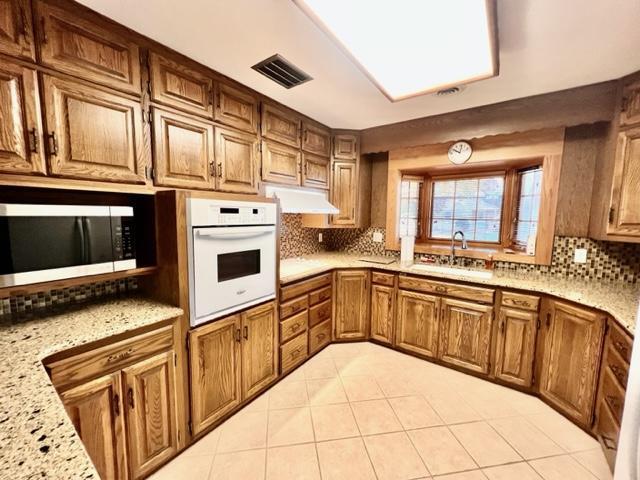 kitchen with tasteful backsplash, sink, light tile patterned flooring, white oven, and light stone counters