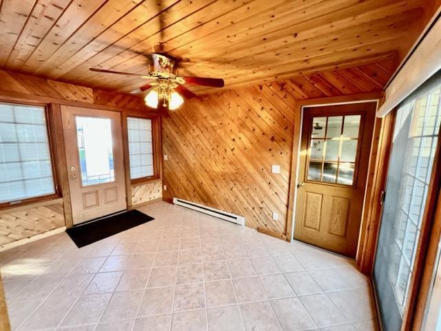 entryway with wood walls, wood ceiling, baseboard heating, light tile patterned floors, and ceiling fan