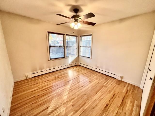 spare room with baseboard heating, light wood-type flooring, and ceiling fan