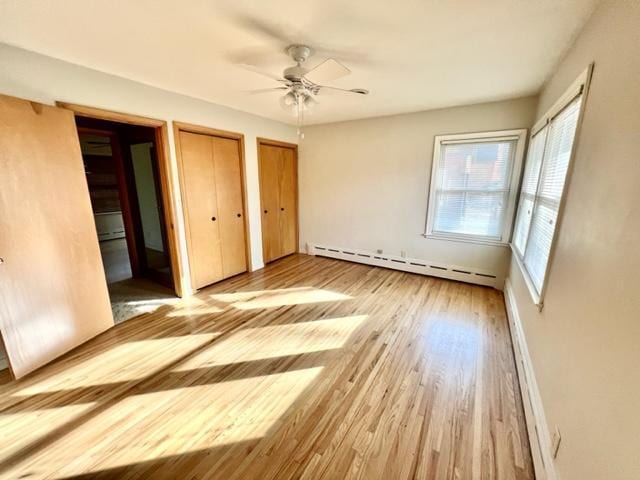 unfurnished bedroom featuring light hardwood / wood-style flooring, a baseboard radiator, two closets, and ceiling fan