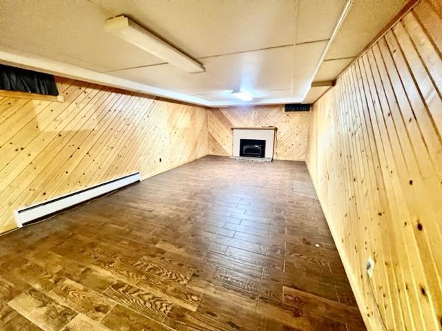 unfurnished living room with baseboard heating, dark wood-type flooring, and wood walls