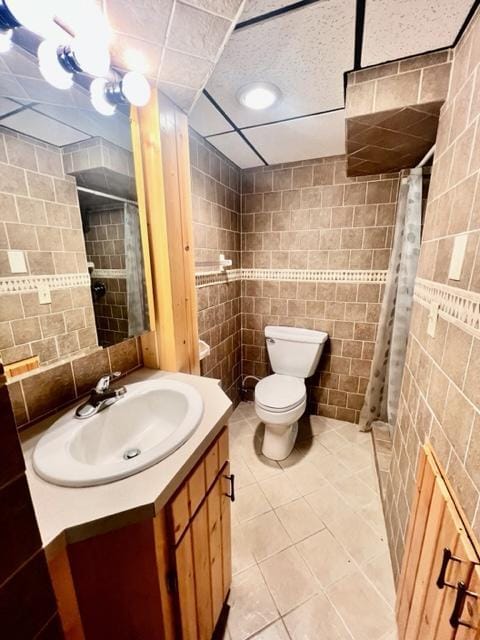 bathroom with a shower with shower curtain, toilet, tile patterned floors, tile walls, and vanity