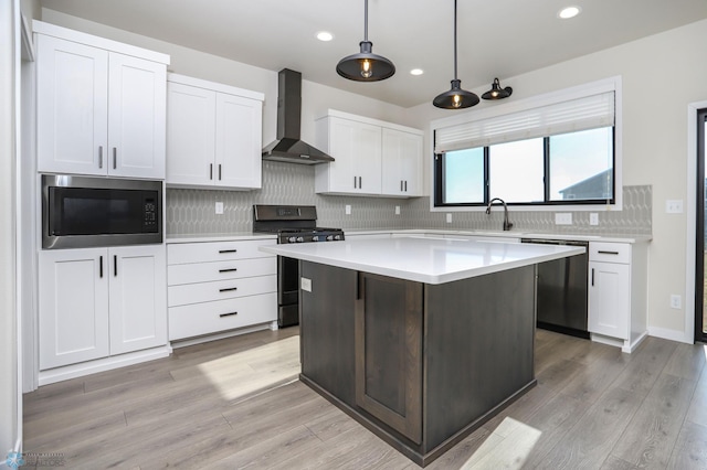 kitchen with wall chimney range hood, appliances with stainless steel finishes, white cabinetry, and pendant lighting