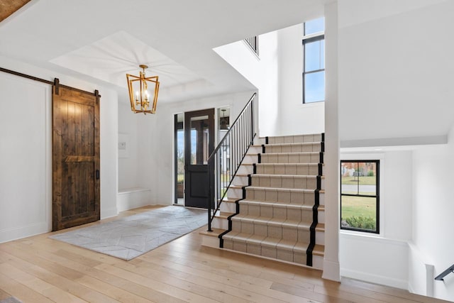 foyer entrance with a raised ceiling, a barn door, light hardwood / wood-style flooring, and a notable chandelier