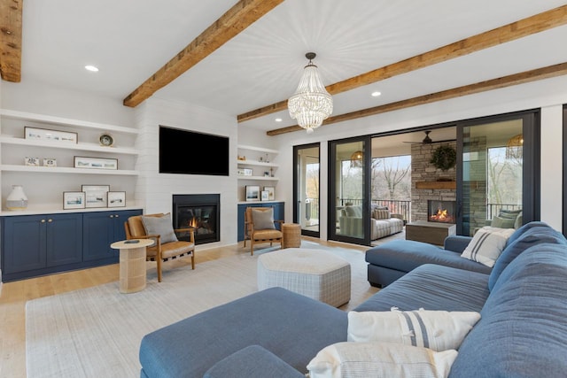 living room with built in shelves, an inviting chandelier, light hardwood / wood-style flooring, beamed ceiling, and a stone fireplace