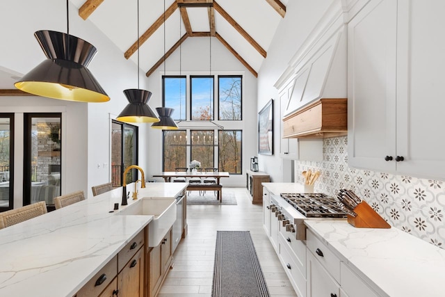 kitchen featuring decorative backsplash, stainless steel gas cooktop, beam ceiling, white cabinets, and hanging light fixtures