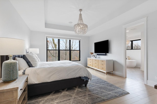 bedroom featuring hardwood / wood-style floors, a notable chandelier, a tray ceiling, and ensuite bath