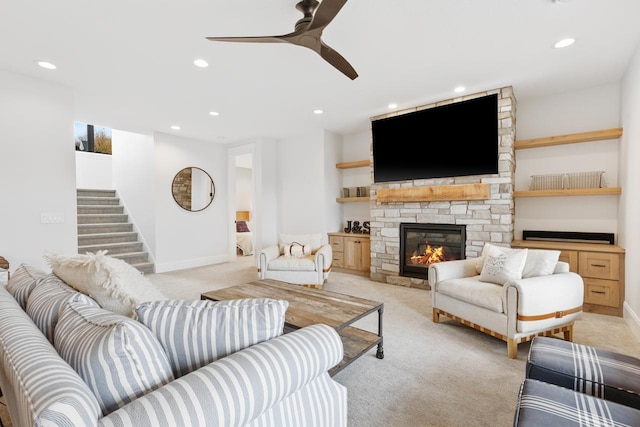 living room featuring a stone fireplace, ceiling fan, and light colored carpet