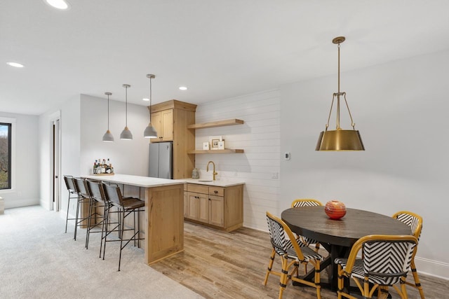 kitchen featuring open shelves, light countertops, hanging light fixtures, freestanding refrigerator, and a sink