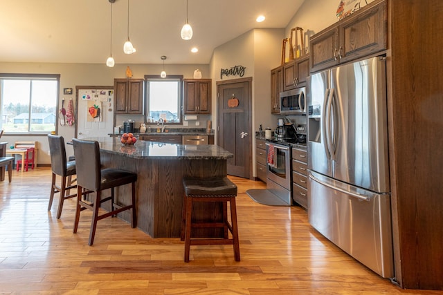 kitchen featuring light hardwood / wood-style floors, lofted ceiling, appliances with stainless steel finishes, and a center island