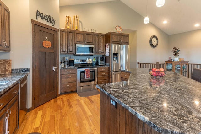 kitchen with stainless steel appliances, vaulted ceiling, pendant lighting, dark stone countertops, and light hardwood / wood-style flooring