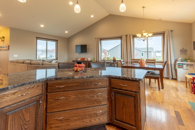 kitchen with light hardwood / wood-style flooring, dark stone countertops, vaulted ceiling, decorative light fixtures, and an inviting chandelier