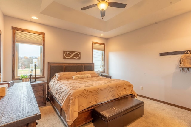 bedroom featuring light carpet, a tray ceiling, multiple windows, and ceiling fan