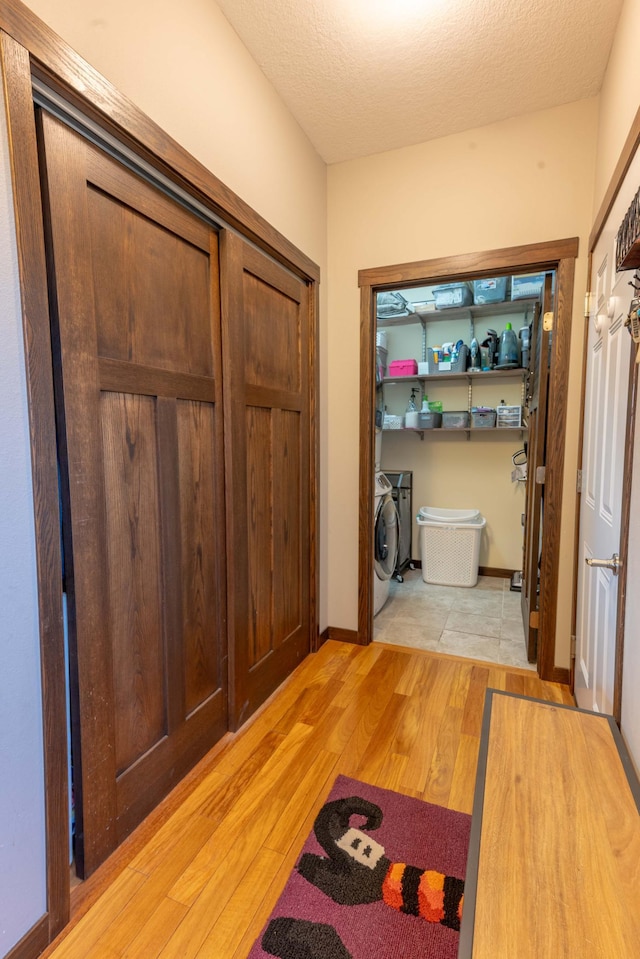 corridor featuring independent washer and dryer, a textured ceiling, and light hardwood / wood-style floors