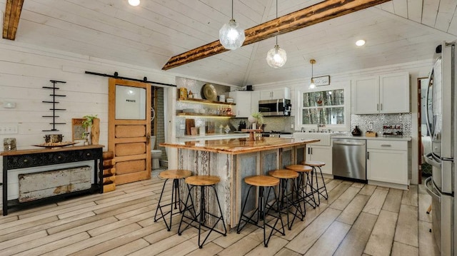 kitchen featuring wooden counters, stainless steel appliances, a barn door, decorative light fixtures, and white cabinets