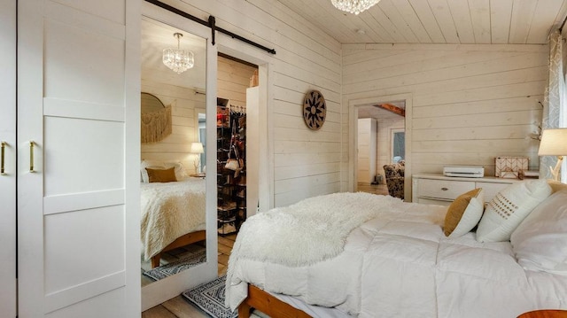 bedroom with a closet, wooden ceiling, vaulted ceiling, a barn door, and wood walls