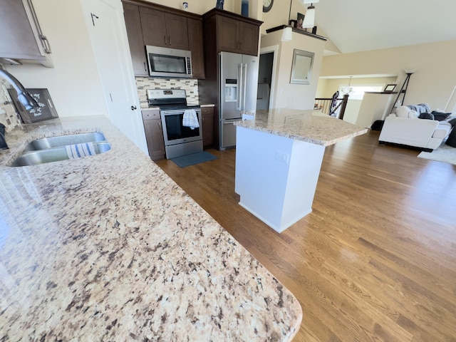 kitchen with appliances with stainless steel finishes, dark hardwood / wood-style flooring, dark brown cabinetry, lofted ceiling, and light stone counters