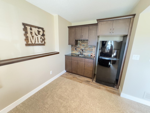 kitchen featuring sink, black refrigerator, light colored carpet, and backsplash