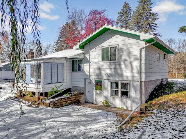 snow covered back of property featuring a sunroom and a patio area