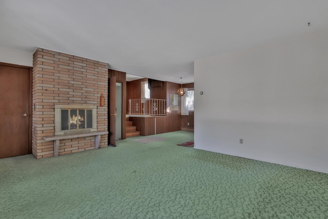 unfurnished living room featuring carpet flooring, a baseboard radiator, wooden walls, and a fireplace