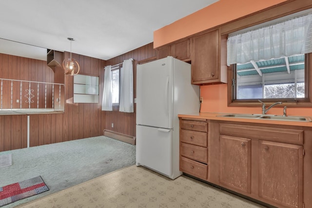 kitchen with wooden walls, sink, white refrigerator, and hanging light fixtures