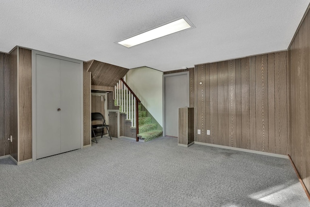 basement featuring light carpet, a textured ceiling, and wood walls