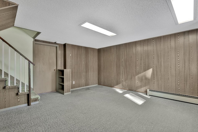 basement with light carpet, a textured ceiling, a baseboard heating unit, and wooden walls