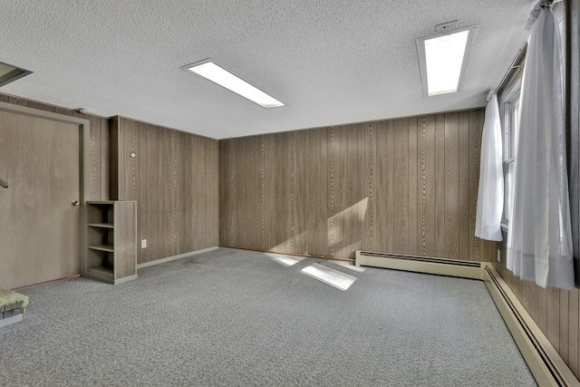 spare room featuring light carpet, wood walls, a textured ceiling, and baseboard heating