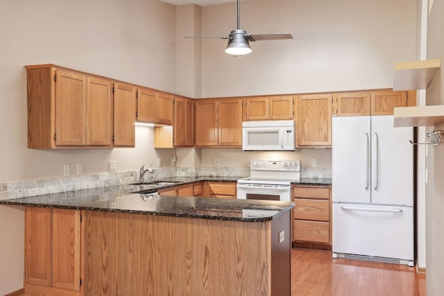 kitchen featuring white appliances, sink, kitchen peninsula, and a high ceiling