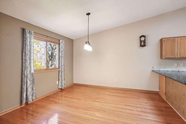 unfurnished dining area featuring light hardwood / wood-style floors, a textured ceiling, and vaulted ceiling