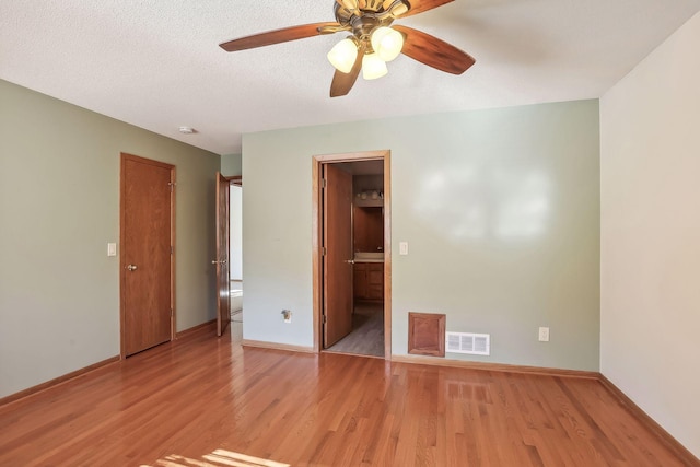 unfurnished bedroom featuring ensuite bathroom, light wood-type flooring, a walk in closet, a textured ceiling, and ceiling fan