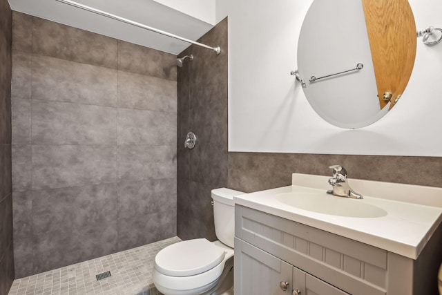 bathroom with a tile shower, toilet, and vanity