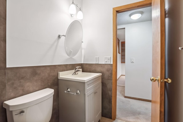 bathroom featuring toilet, a textured ceiling, vanity, and tile walls