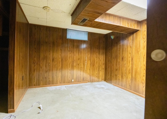 basement with a paneled ceiling and wood walls