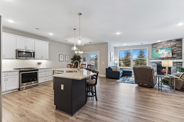 kitchen with a kitchen island with sink, white cabinets, sink, decorative light fixtures, and stainless steel appliances