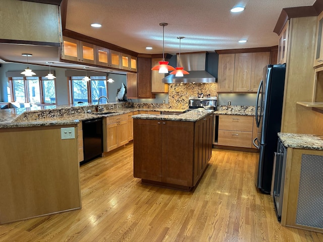 kitchen with refrigerator, wall chimney range hood, black dishwasher, decorative light fixtures, and a center island