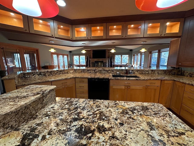 kitchen featuring dishwasher, sink, hanging light fixtures, dark stone countertops, and a fireplace